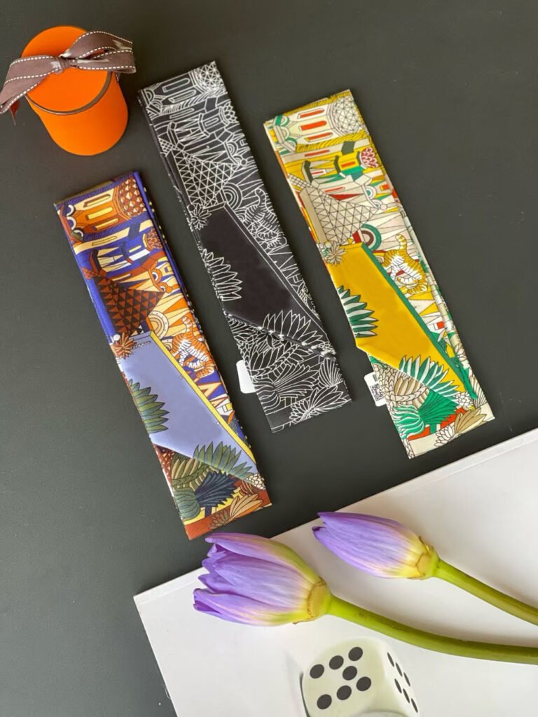 A luxurious multicolor printed silk twilly scarf tied around the handle of a leather handbag, showcasing its versatility as a fashion accessory.