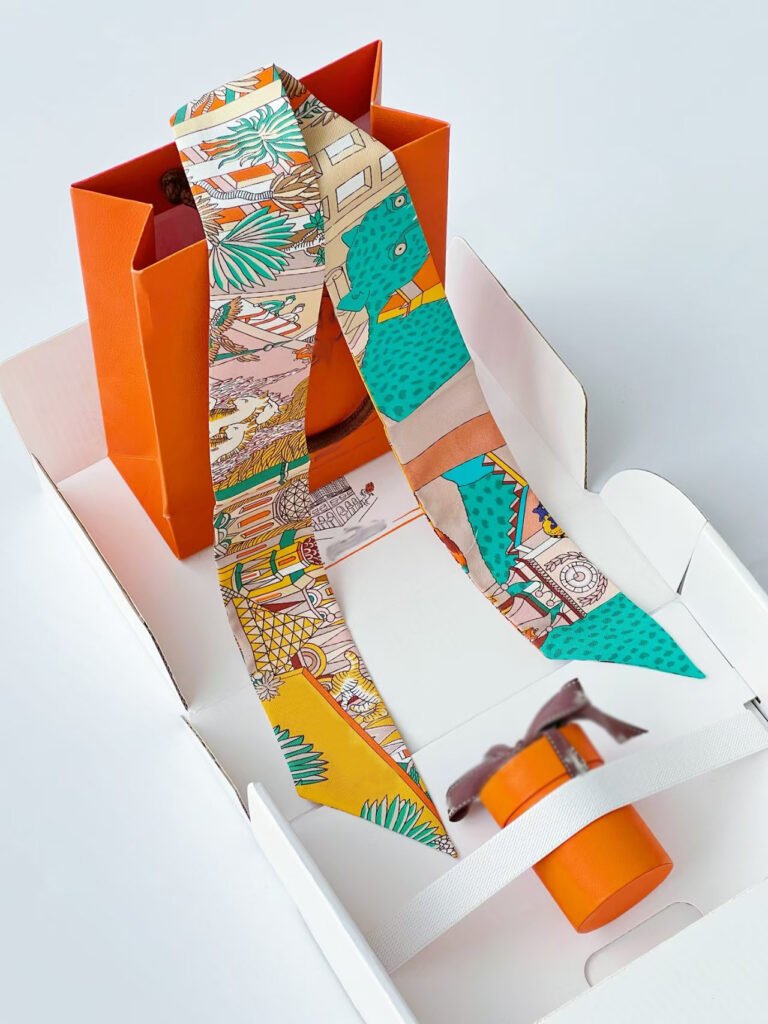 A luxurious multicolor printed silk twilly scarf tied around the handle of a leather handbag, showcasing its versatility as a fashion accessory.