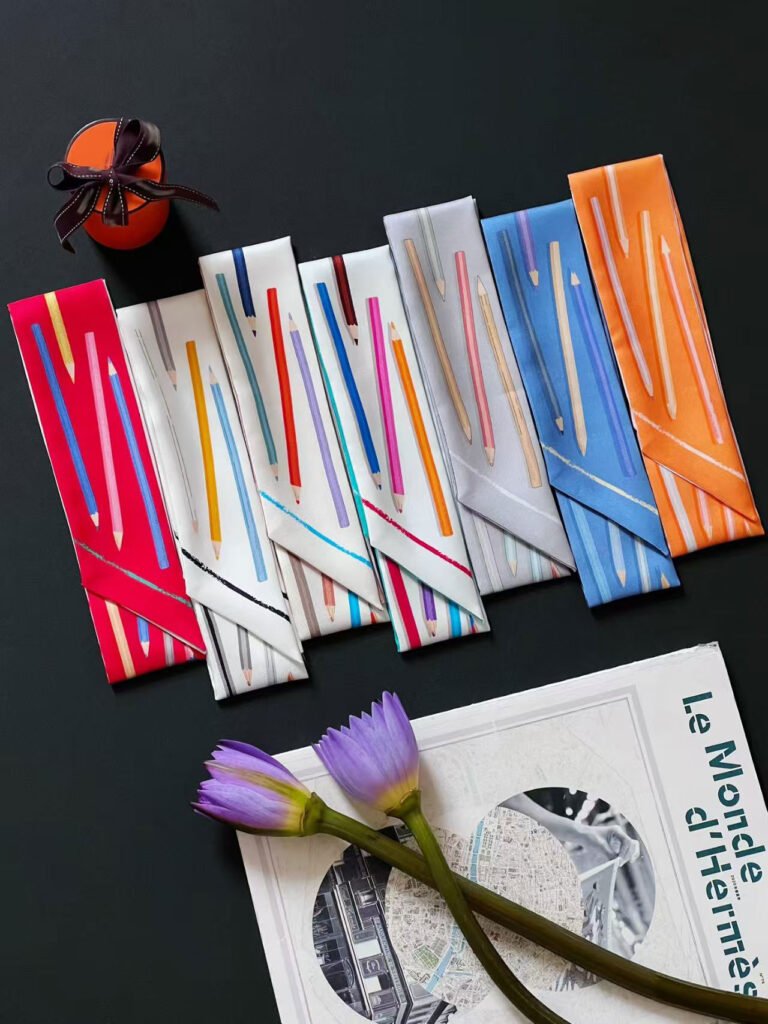 A luxurious multicolor printed silk twilly scarf tied around the handle of a leather handbag, showcasing its versatility as a fashion accessory.