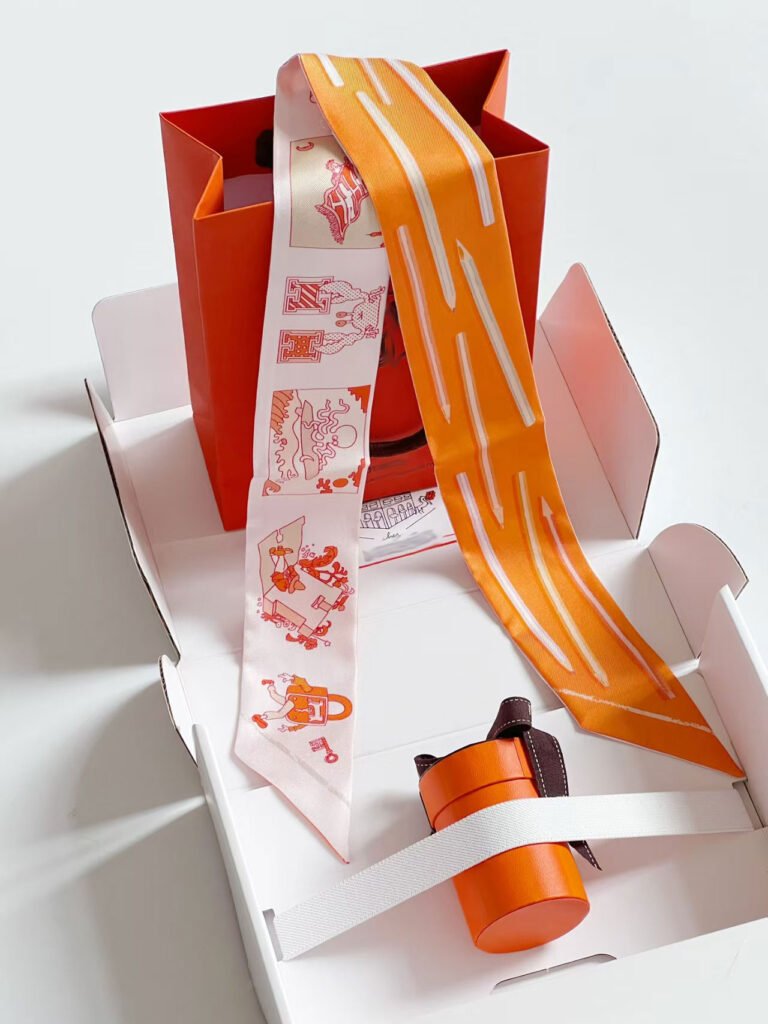 A luxurious multicolor printed silk twilly scarf tied around the handle of a leather handbag, showcasing its versatility as a fashion accessory.